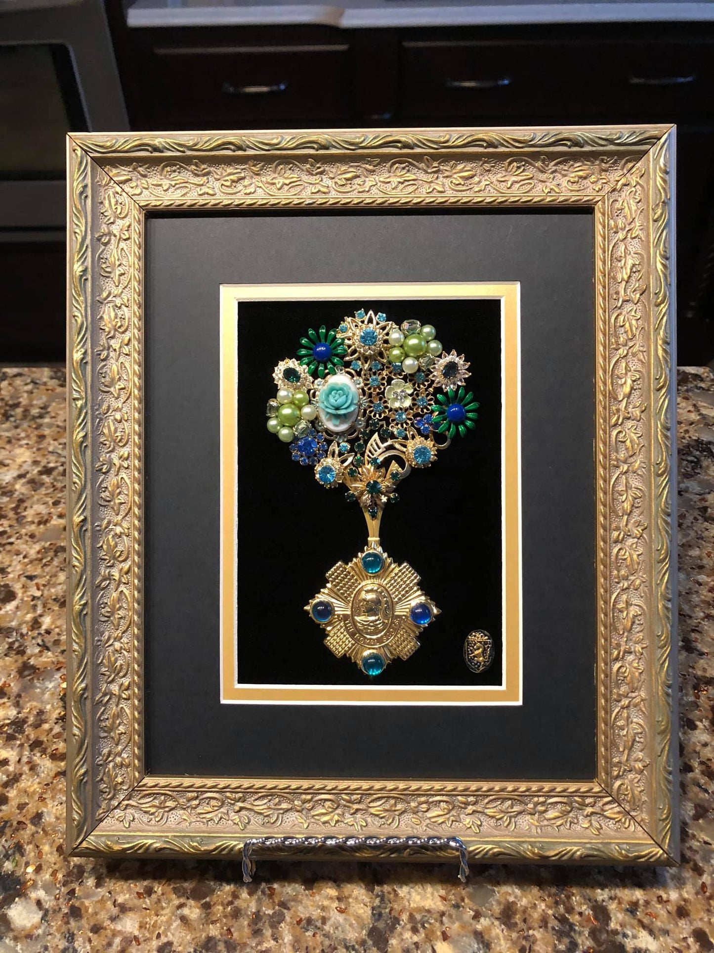 Decorative art piece made of vintage jewelry with floral motif and rhinestones on velvet in a gold frame