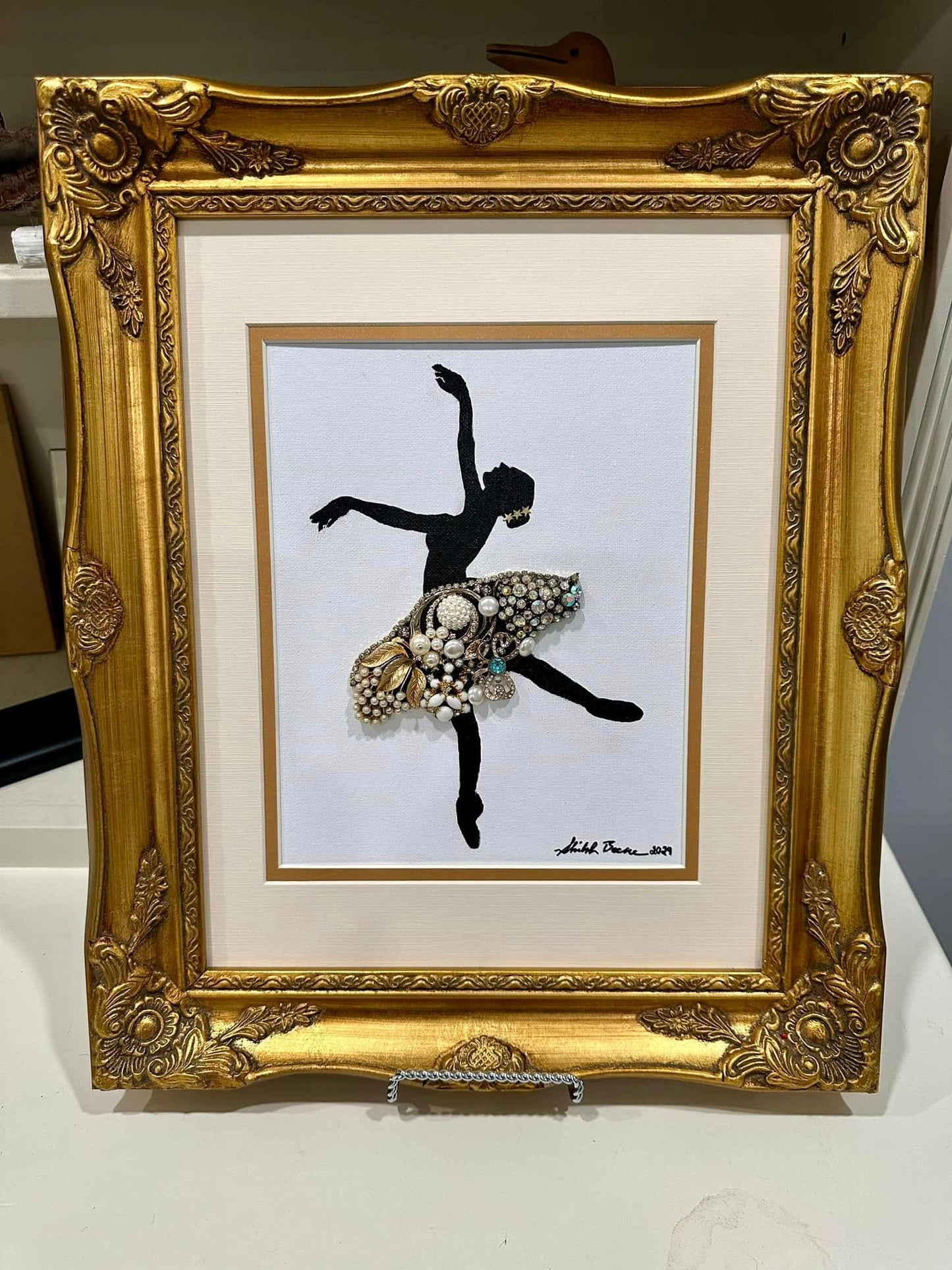 artwork of the silouette of a ballerina made from vintage jewelry on a white background in a golden frame