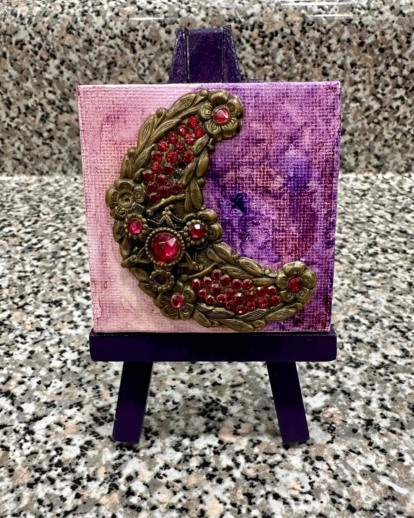 Decorative moon brooch with pink gemstones on a small easel