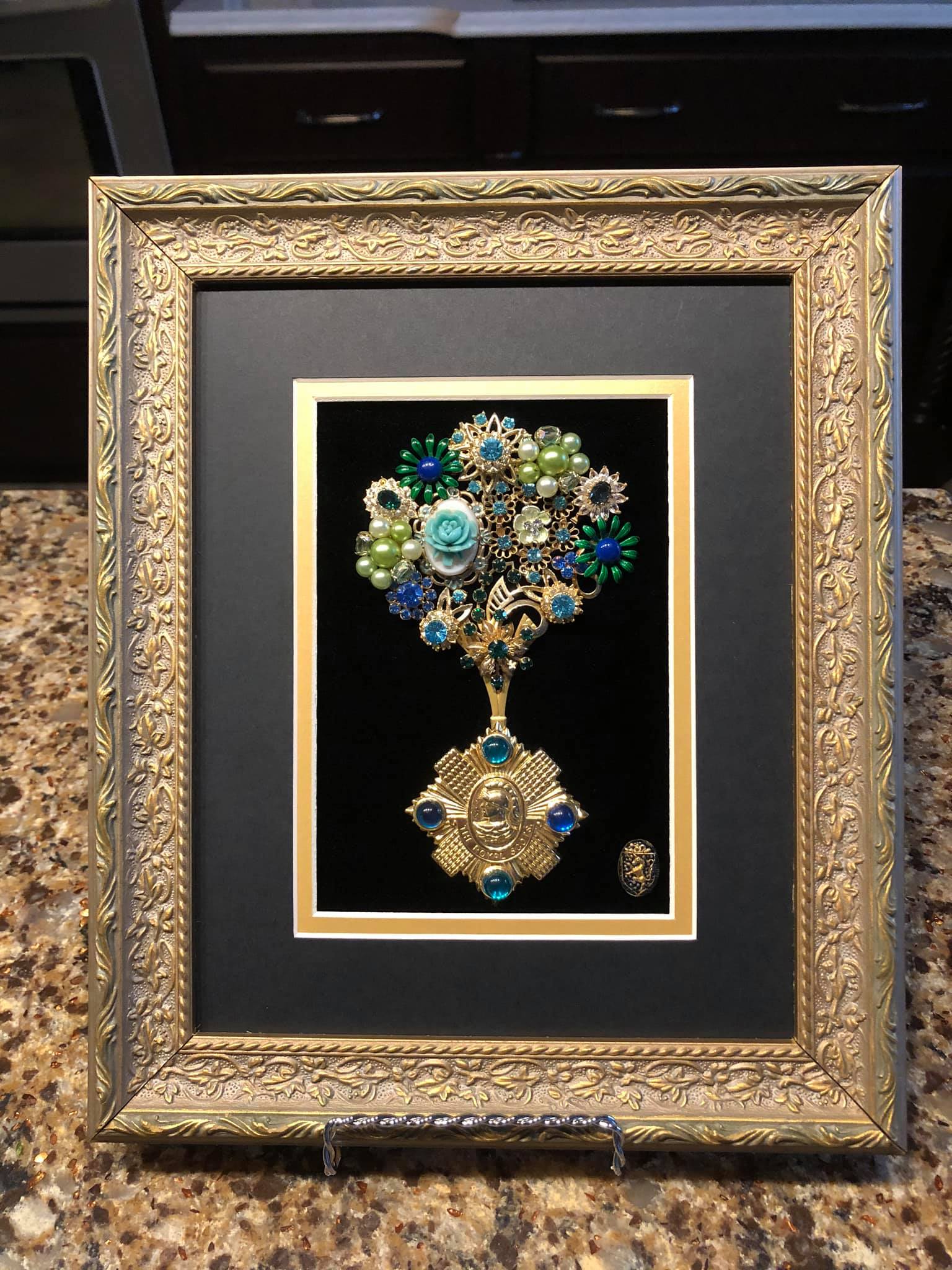 Decorative art piece made of vintage jewelry with  floral motif and rhinestones on velvet in a gold frame 