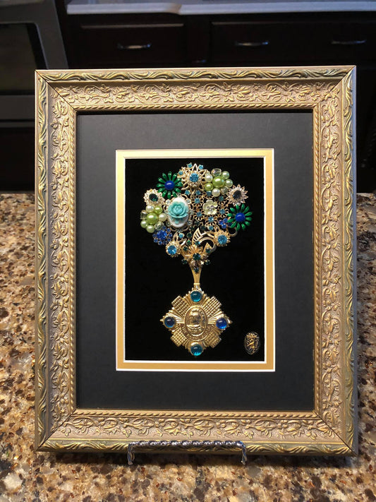 Decorative art piece made of vintage jewelry with  floral motif and rhinestones on velvet in a gold frame 