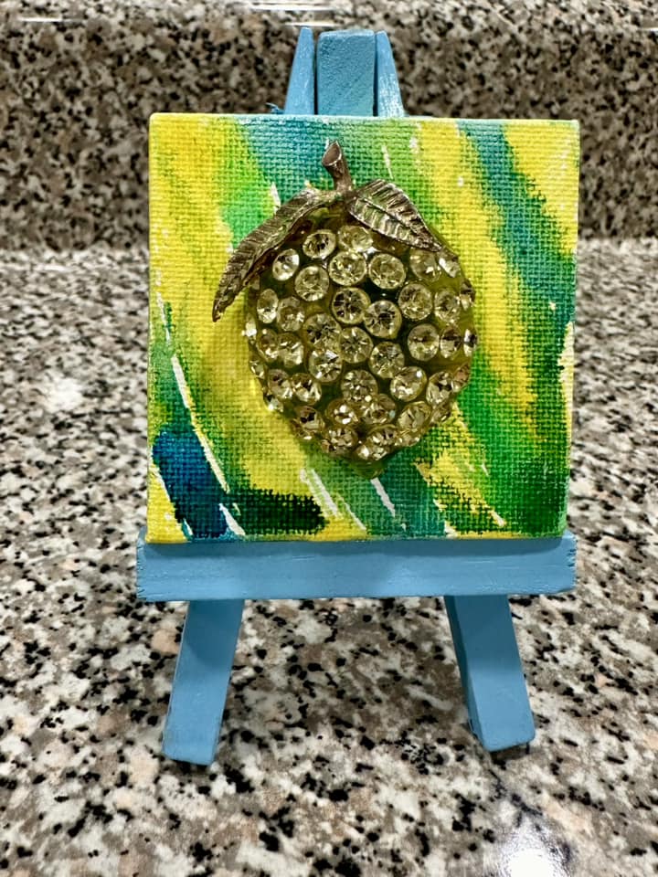 Decorative brooch of a lemon on a small canvas with original art background in yellow and green, on a small easel 