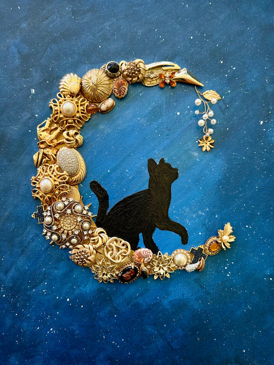 playful black cat on crescent moon made of vintage jewelry pieces on blue backround