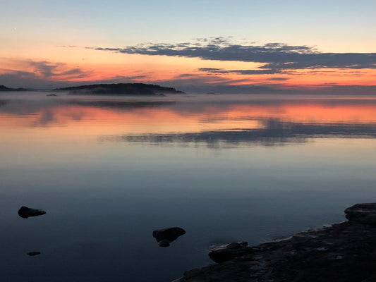 Misty Lake Superior at sunset with silhouettes of rocks and distant landforms.