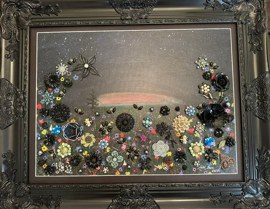Decorative artwork with vintage jewelry, flowers and a landscape in an ornate black frame.