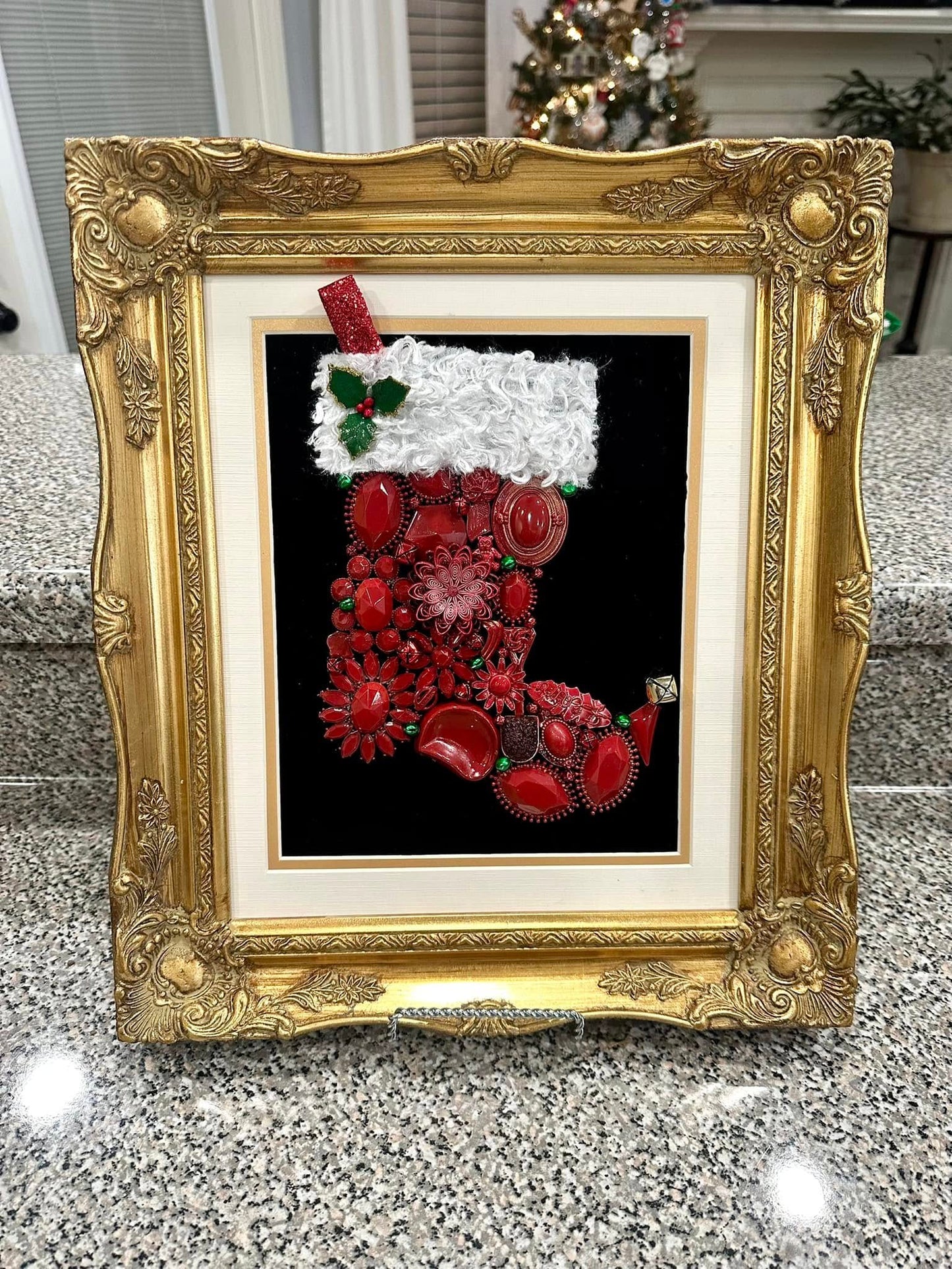 Decorative Christmas stocking made from vintage jewelry with red and white colors framed in an ornate gold frame.