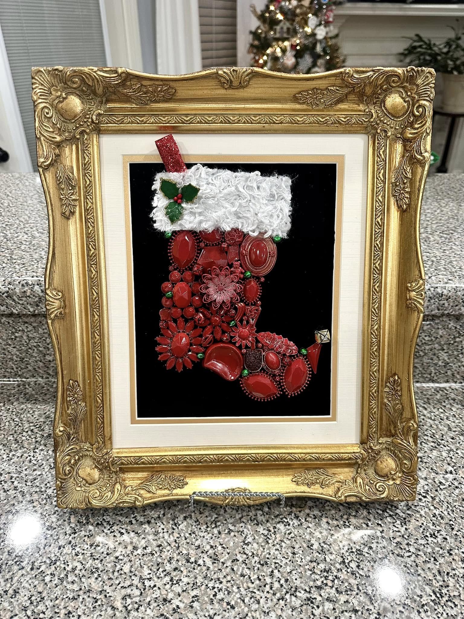 Decorative Christmas stocking made from vintage jewelry with red and white colors framed in an ornate gold frame.