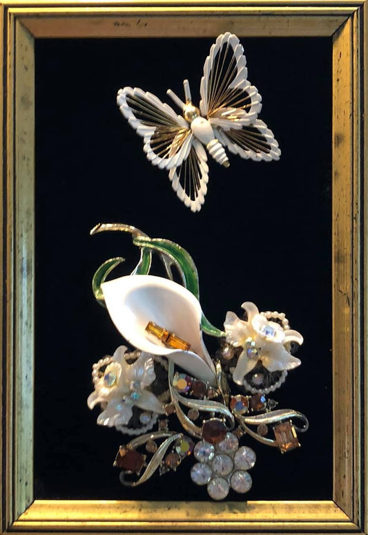 Butterfly and floral brooches in a gold frame on a black velvet background