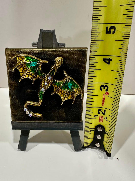 Dragon-shaped brooch on 2.5" x 2.5" canvas with original art backfround on a mini-easel, with a ruler for scale