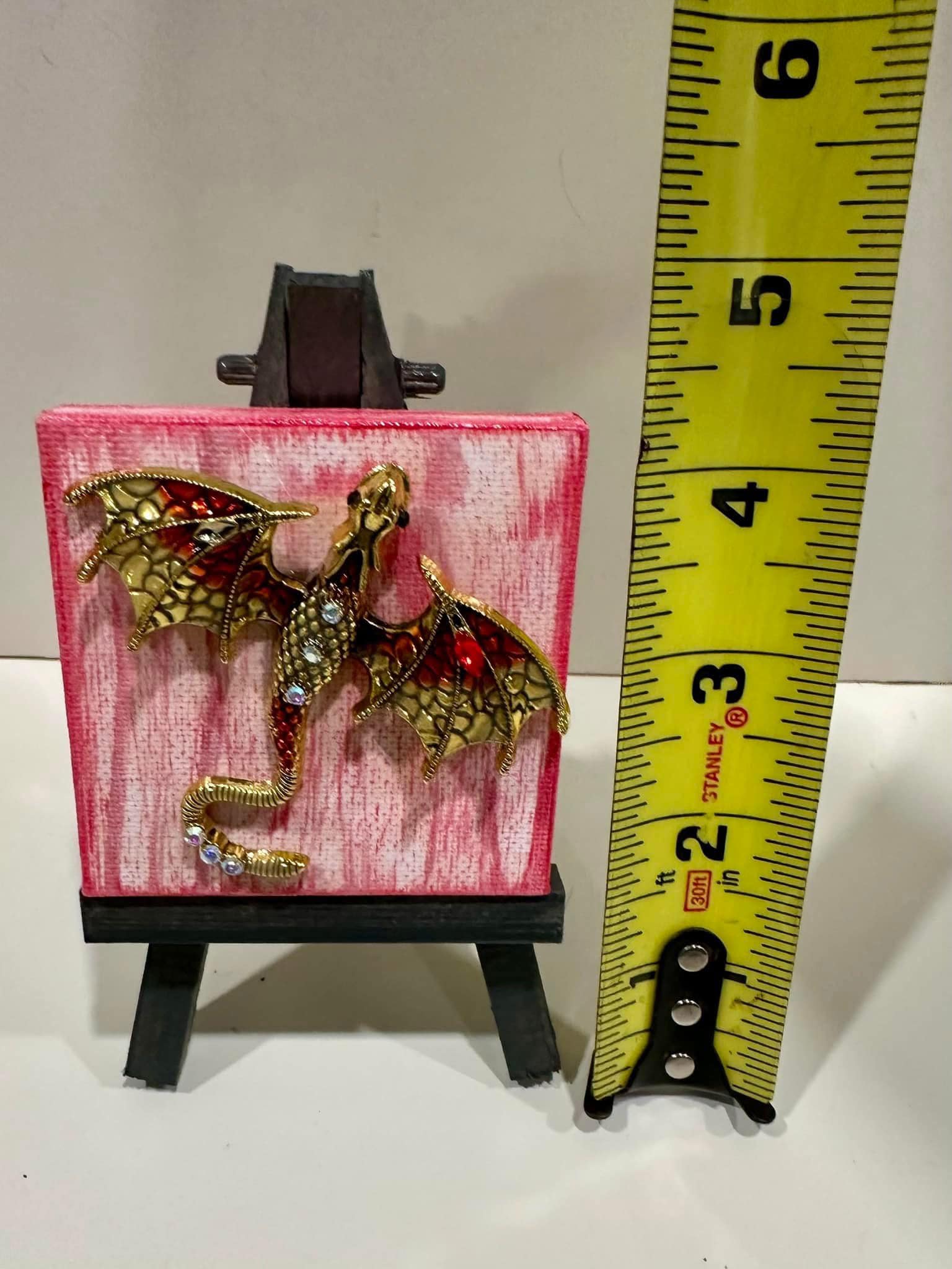 Decorative dragon brooch with red and white background on small easel 